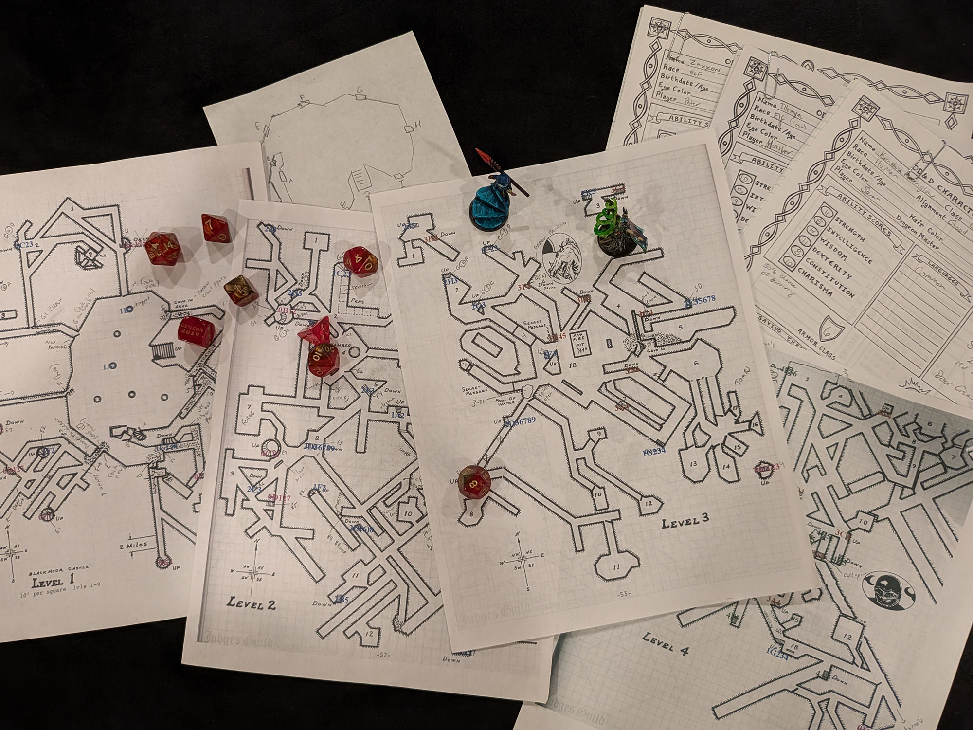 Maps of the dungeons of Castle Blackmoor, character sheets, dice, and miniature spread across a gaming table.